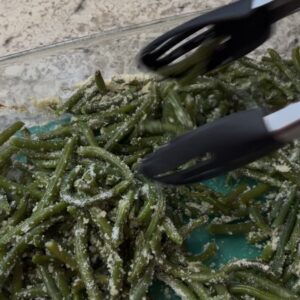 roasted garlic and parmesan green beans being mixed with tongs