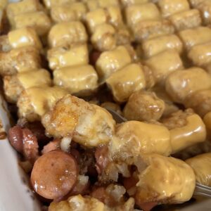 close up picture of beef, bean, and hot dog mixture with cheesy tator tots on top in baking dish