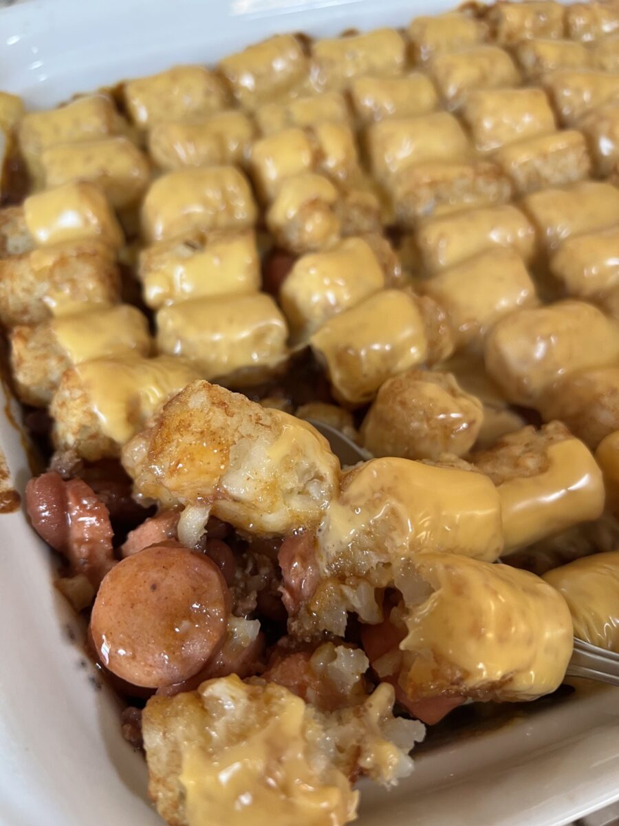 close up picture of beef, bean, and hot dog mixture with cheesy tator tots on top in baking dish