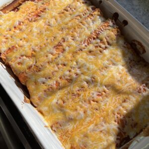 baking dish with chicken and black bean enchiladas topped with melted colby jack cheese
