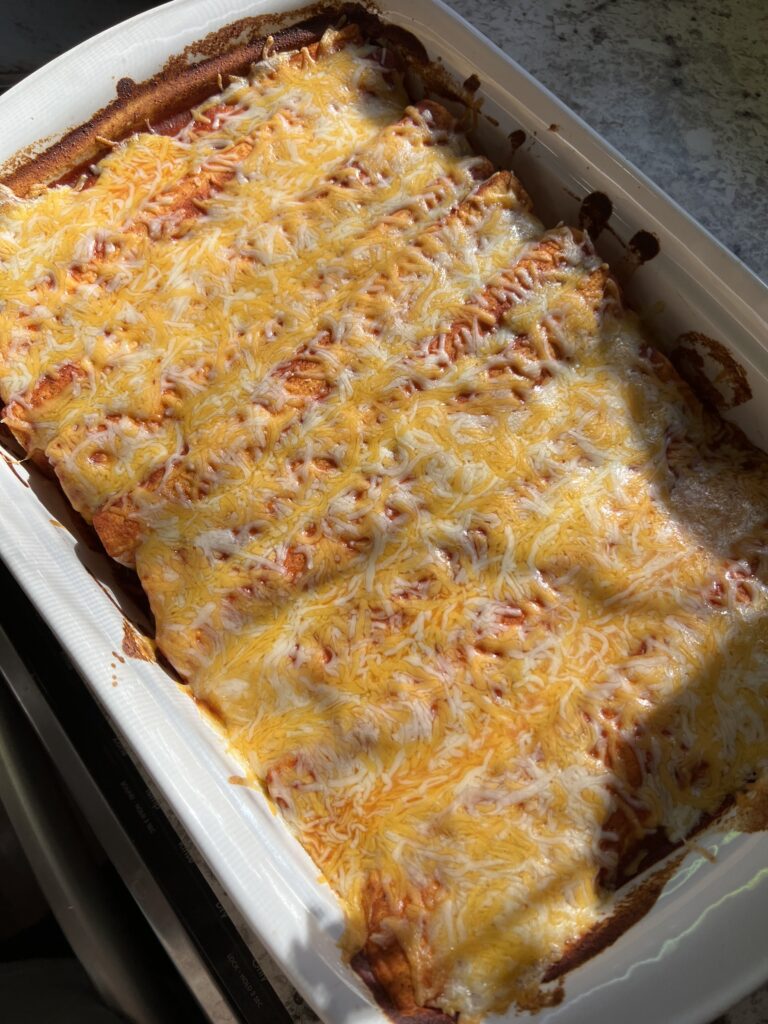 baking dish with chicken and black bean enchiladas topped with melted colby jack cheese