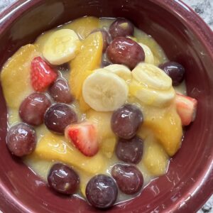 canned peaches, strawberries, red seedless grapes, and sliced banana fruit salad in burgundy bowl