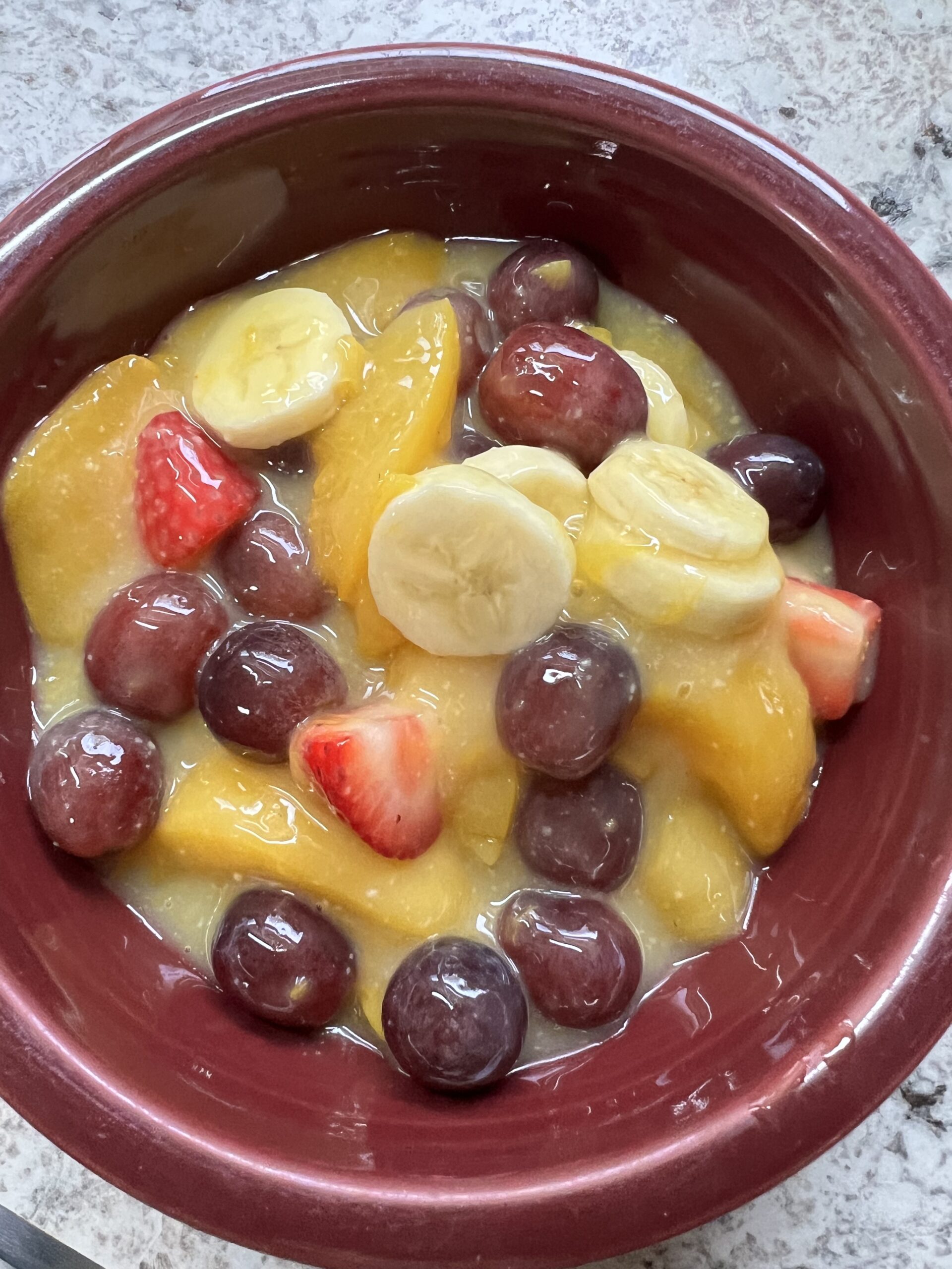 canned peaches, strawberries, red seedless grapes, and sliced banana fruit salad in burgundy bowl