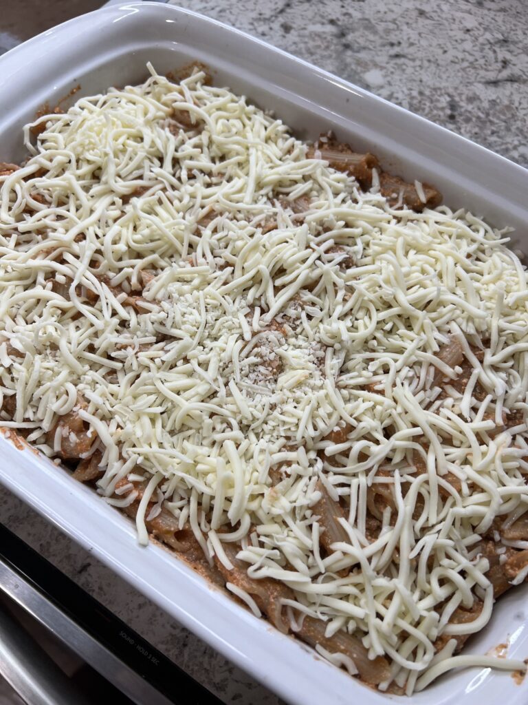 mozzarella cheese topped on cooked pasta ready to broil