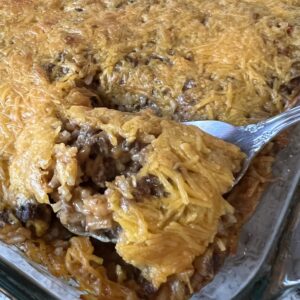 metal serving spoon scooping cheesy hamburger rice out of baking dish