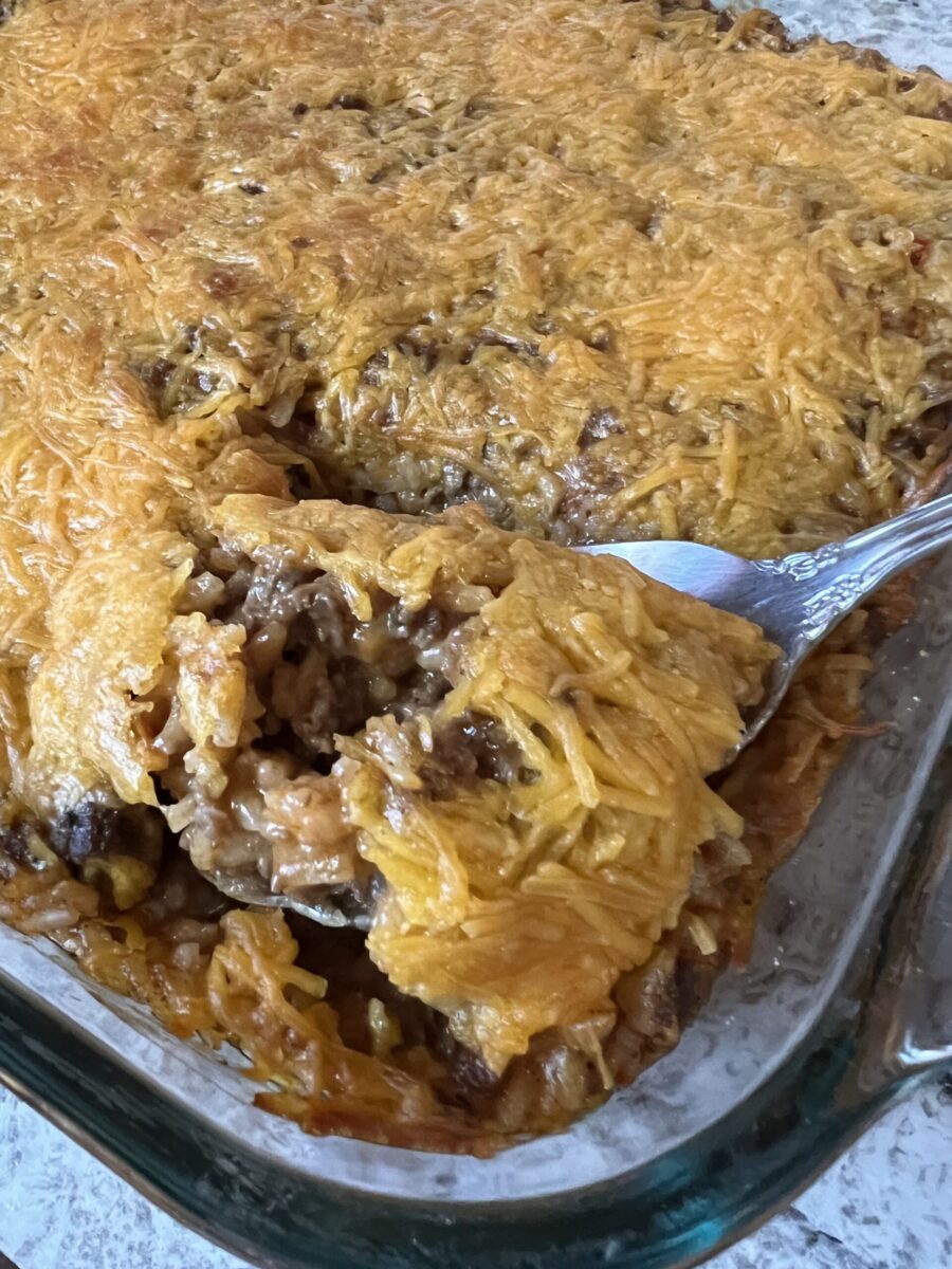 metal serving spoon scooping cheesy hamburger rice out of baking dish